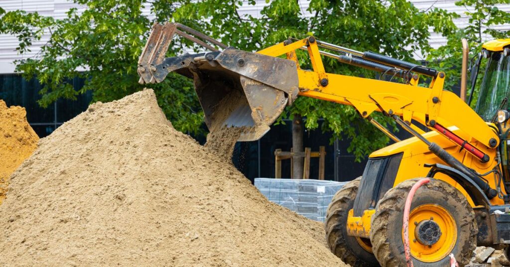Grävmaskin som flyttar sand vid markarbete på byggarbetsplats