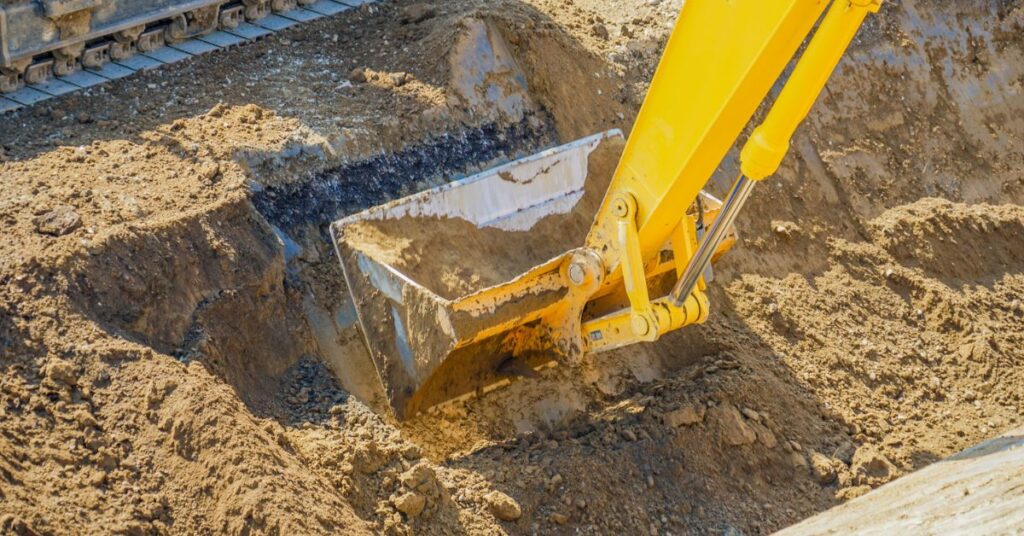 Grävmaskin som gräver schakt för dränering och markarbete vid husgrund